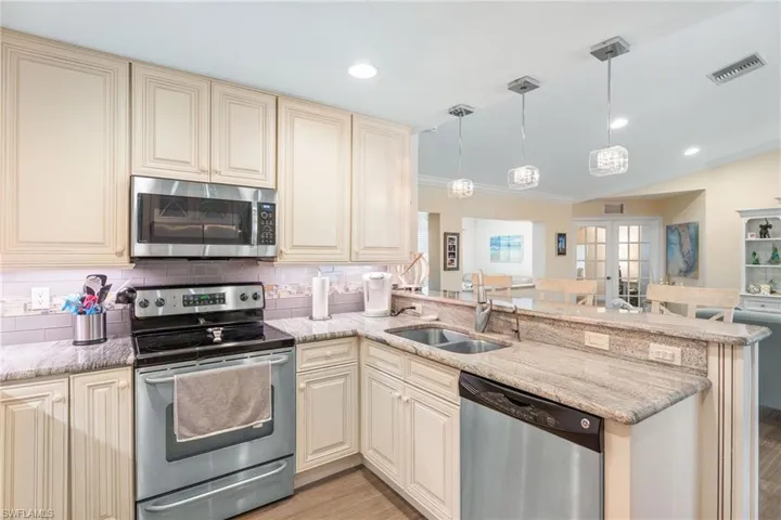 Kitchen featuring stainless steel appliances, cream cabinets, a sink, a peninsula, and light wood-style flooring