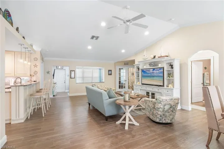 Living room featuring crown molding, arched walkways, ceiling fan, baseboards, and lofted ceiling