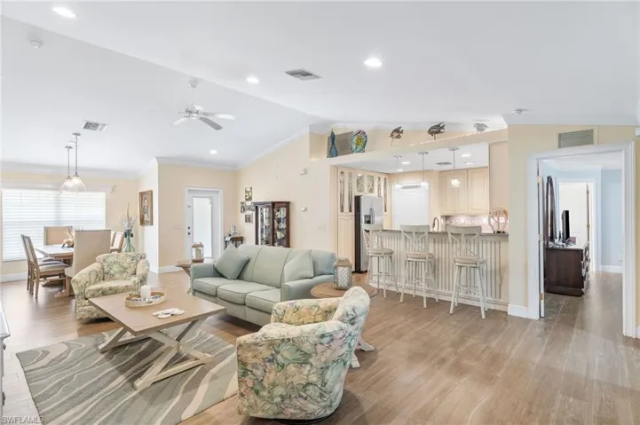 Living room featuring vaulted ceiling, ornamental molding, light wood-type flooring, baseboards, and a ceiling fan