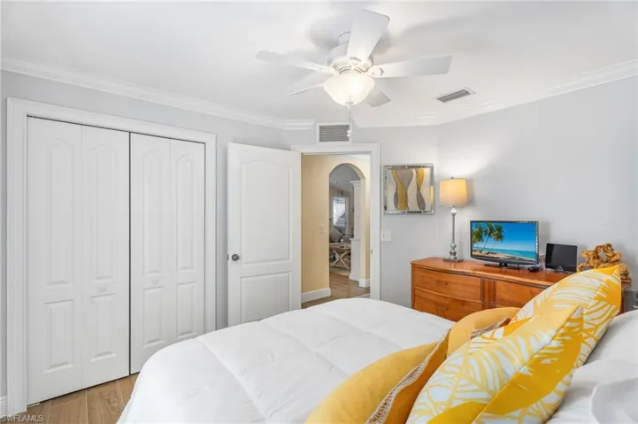 Bedroom with arched walkways, a closet, wood finished floors, ornamental molding, and a ceiling fan