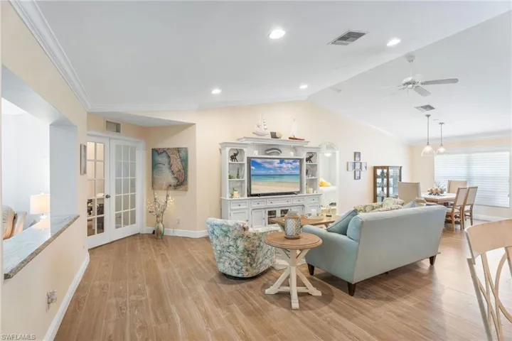 Living room featuring french doors, baseboards, light wood-type flooring, crown molding, and vaulted ceiling