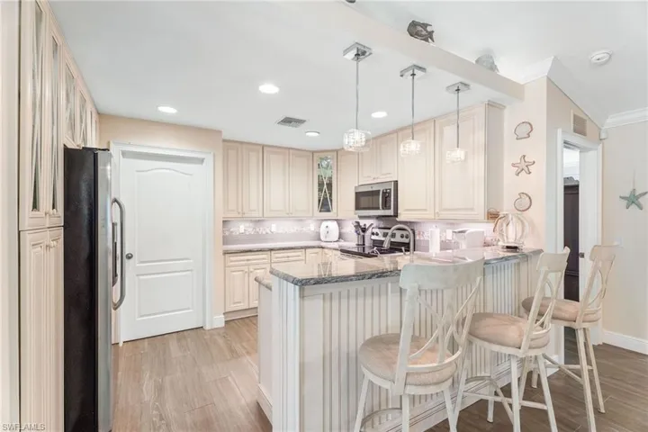 Kitchen featuring appliances with stainless steel finishes, a peninsula, light wood-style flooring, glass insert cabinets, and ornamental molding