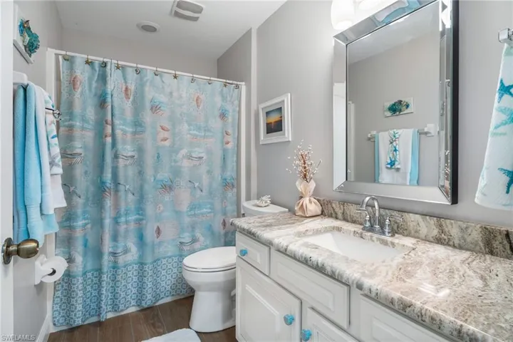 Bathroom with wood finished floors, vanity, toilet, and curtained shower