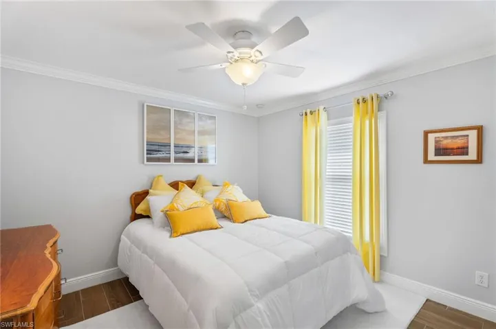 Bedroom with wood finished floors, baseboards, ornamental molding, and ceiling fan
