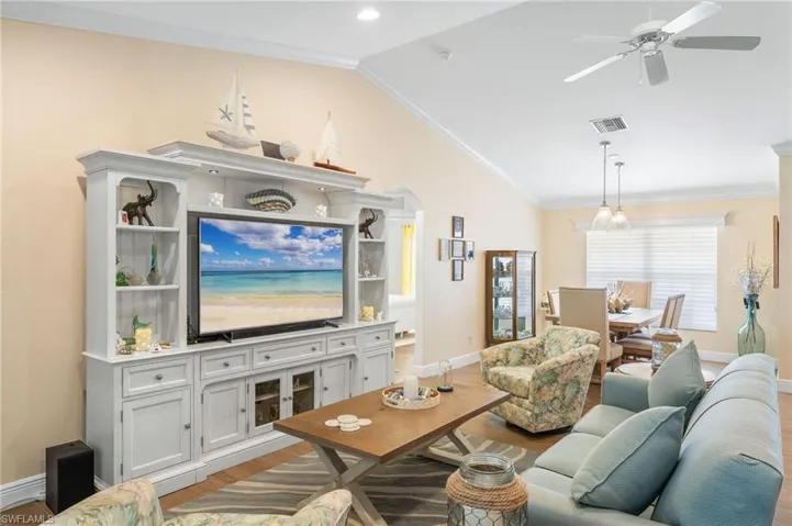 Living room featuring lofted ceiling, wood finished floors, ceiling fan, baseboards, and crown molding