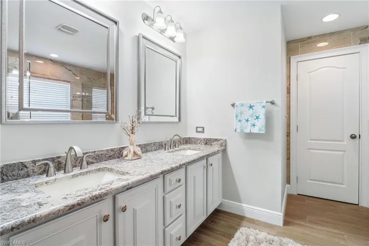 Bathroom featuring double vanity, wood finished floors, baseboards, and a shower