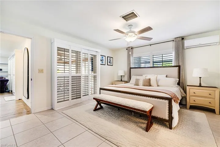 Bedroom featuring a wall unit AC, light tile patterned floors, and a ceiling fan