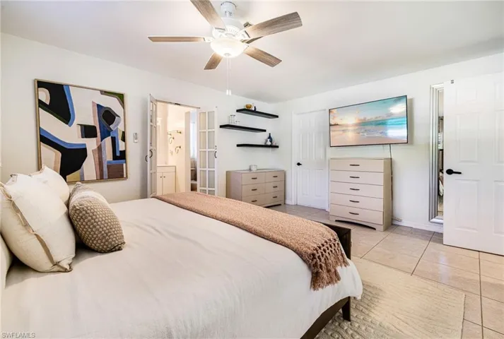 Bedroom with light tile patterned floors, ceiling fan, and ensuite bath