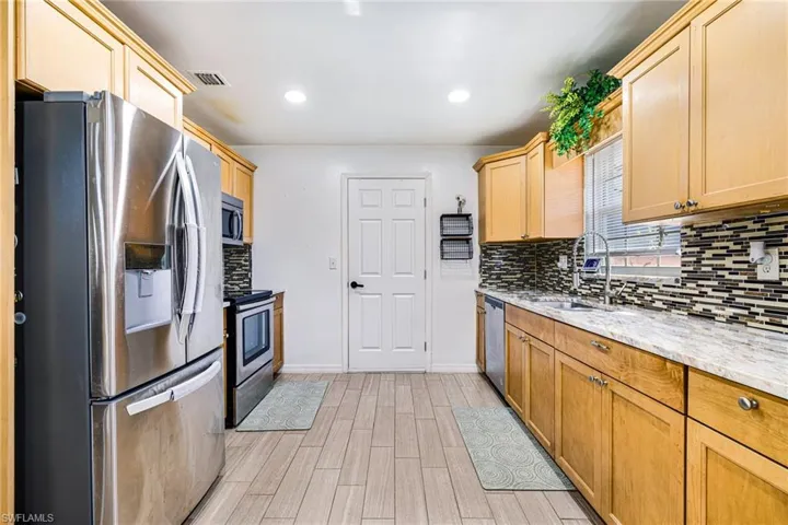 Kitchen with appliances with stainless steel finishes, backsplash, light wood-style flooring, recessed lighting, and light stone countertops
