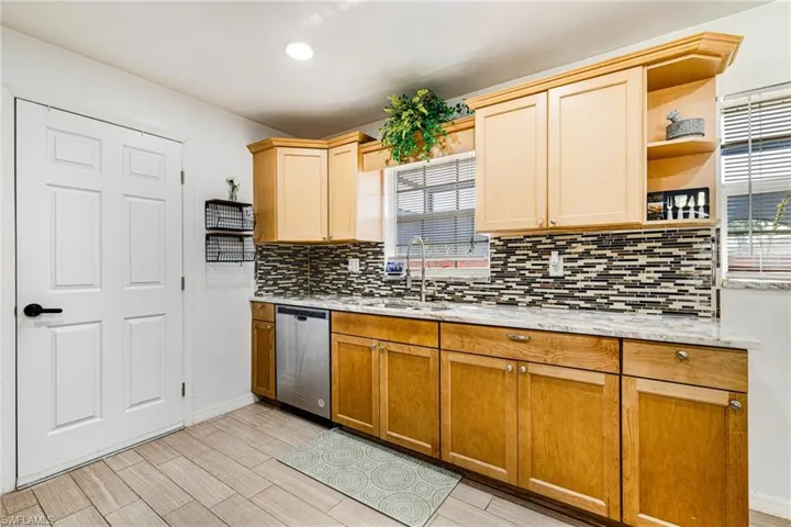 Kitchen featuring stainless steel dishwasher, decorative backsplash, healthy amount of natural light, light wood-style flooring, and recessed lighting