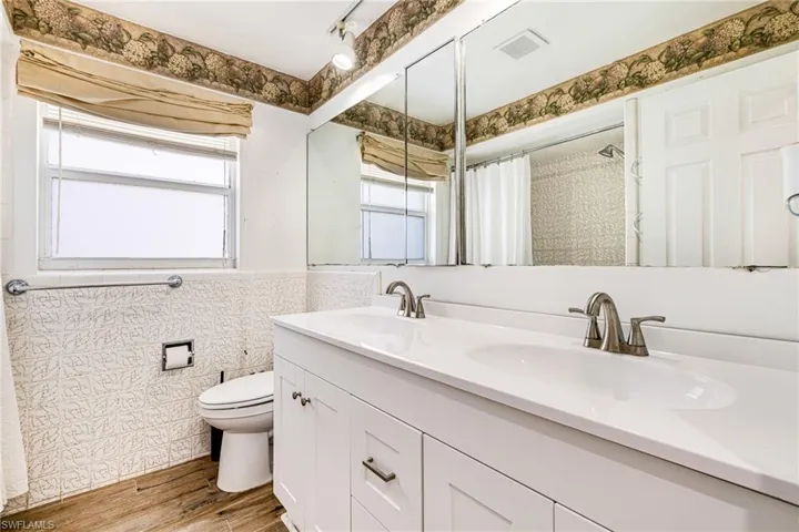 Bathroom with double vanity, tile walls, wood finished floors, a wainscoted wall, and curtained shower