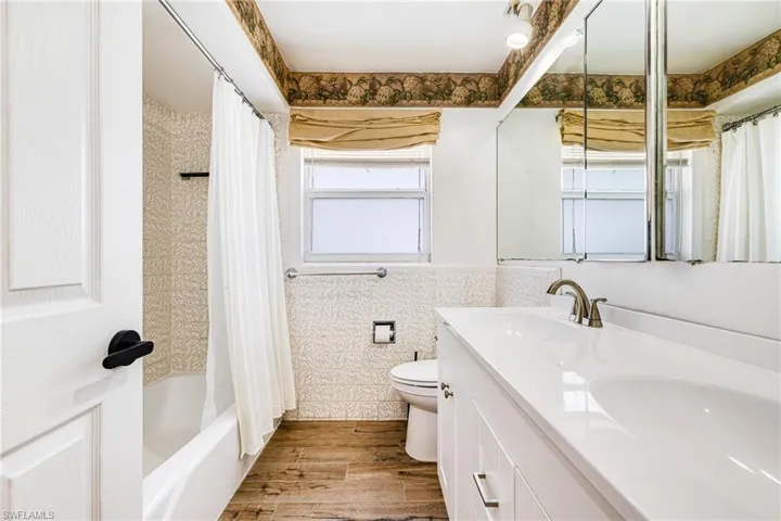 Bathroom with double vanity, wood finished floors, and shower / bathtub combination with curtain
