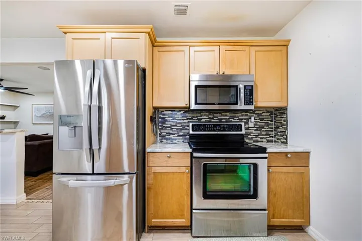 Kitchen featuring stainless steel appliances, tasteful backsplash, light brown cabinetry, and light wood-style flooring