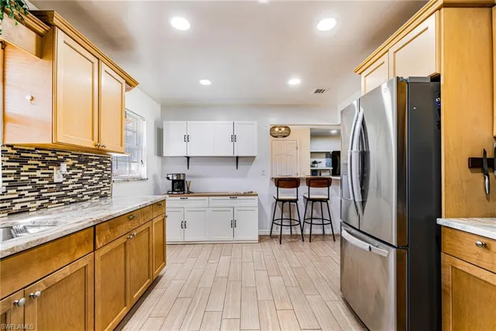 Kitchen featuring stainless steel refrigerator with ice dispenser, backsplash, light countertops, light wood finished floors, and recessed lighting