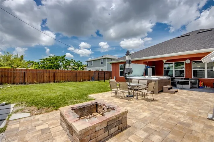 Fenced backyard with a hot tub, a fire pit, a patio, a gazebo, and outdoor dining space