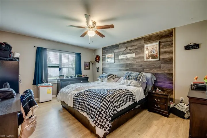 Bedroom featuring an accent wall, light wood finished floors, ceiling fan, and wood walls