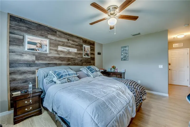 Bedroom featuring an accent wall, wooden walls, wood finished floors, and a ceiling fan