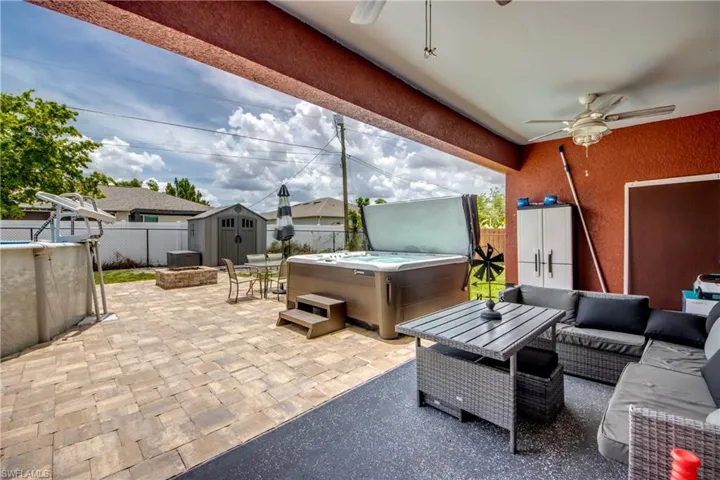Fenced backyard with a hot tub, ceiling fan, a patio, a storage unit, and an outdoor hangout area