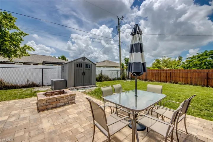 Fenced backyard featuring a storage unit, a patio, a fire pit, and outdoor dining space