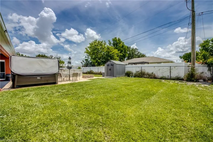 Fenced backyard with a hot tub, a storage unit, and a patio area