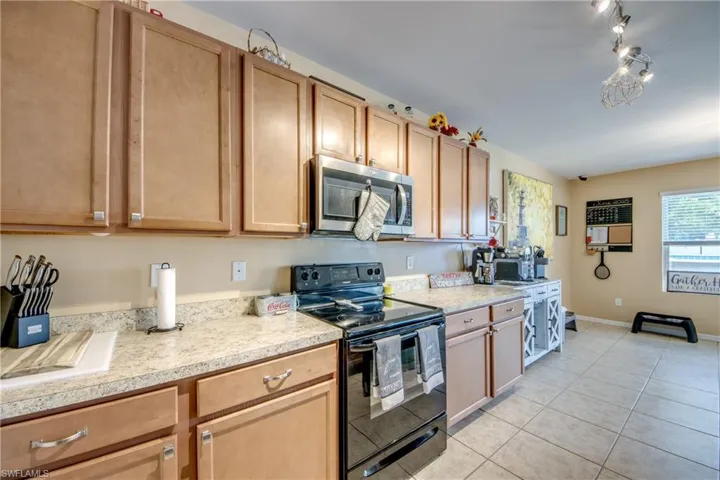 Kitchen featuring stainless steel microwave, black / electric stove, light countertops, and light tile patterned flooring