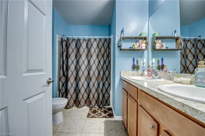 Full bath featuring double vanity, tile patterned floors, and a shower with shower curtain