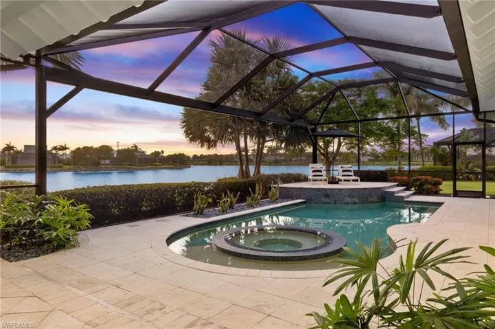 Pool at dusk with an in ground hot tub, a water view, a patio, and a lanai