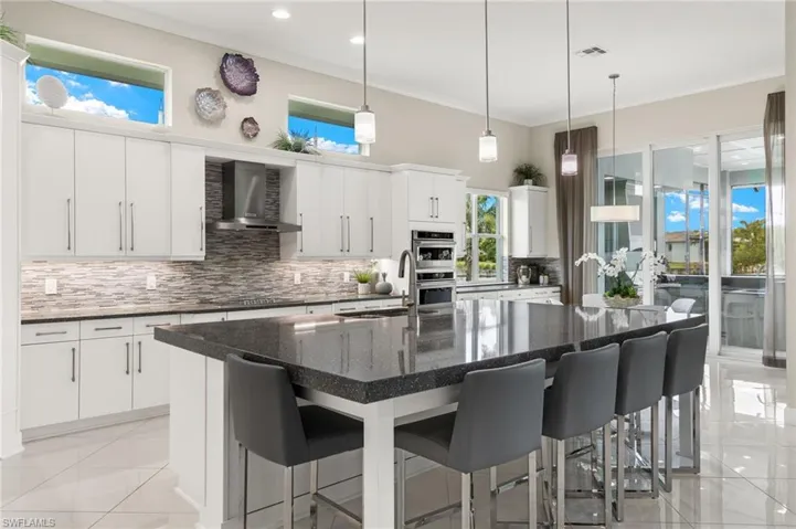 Kitchen with white cabinets, light tile patterned floors, decorative backsplash, exhaust hood, and an island with sink