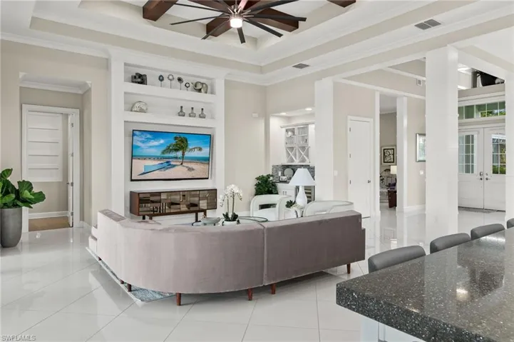 Living room featuring ceiling fan, built in shelves, crown molding, a raised ceiling, and light tile patterned floors