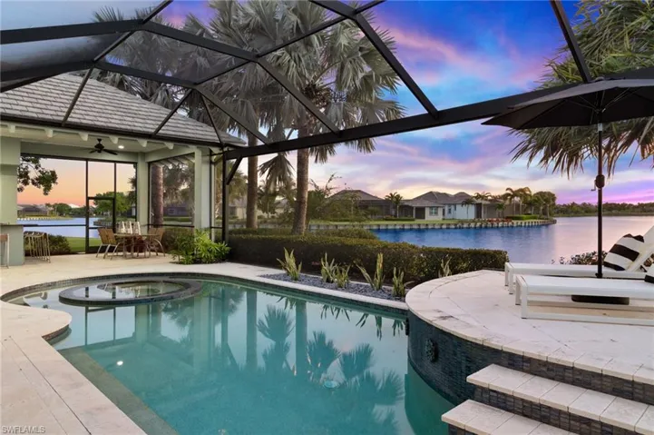 Pool at dusk featuring a patio area, ceiling fan, an in ground hot tub, a water view, and glass enclosure