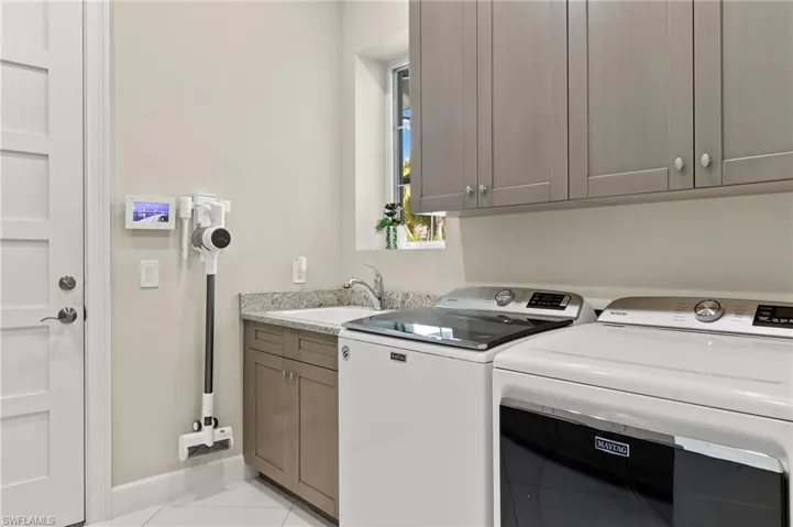 Clothes washing area featuring cabinets, washer and clothes dryer, sink, and light tile patterned floors