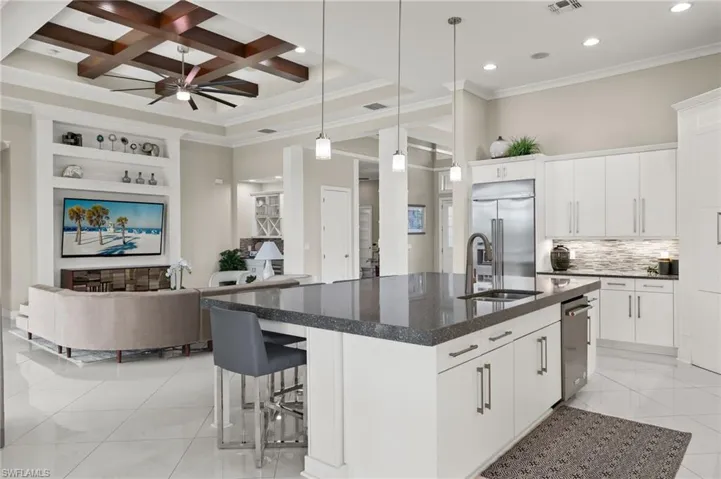 Kitchen with light tile patterned floors, a kitchen island with sink, ceiling fan, coffered ceiling, and appliances with stainless steel finishes