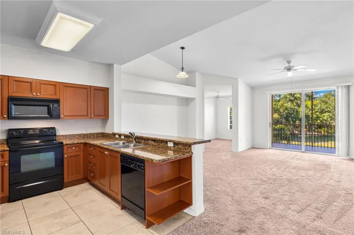 Kitchen featuring black appliances, brown cabinets, a peninsula, open floor plan, and dark stone counters