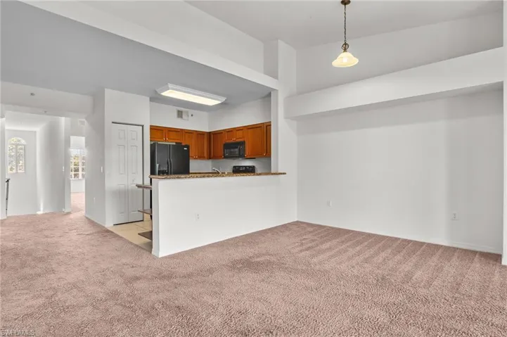 Kitchen featuring light carpet, brown cabinetry, hanging light fixtures, open floor plan, and black appliances