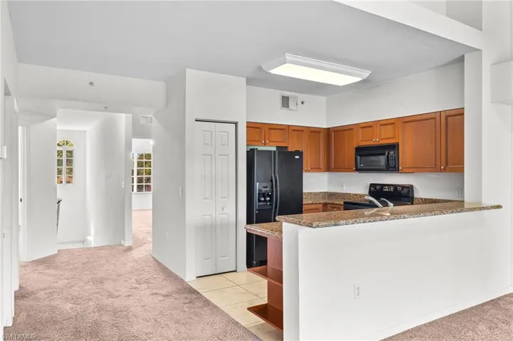 Kitchen featuring light colored carpet, open shelves, brown cabinetry, and black appliances