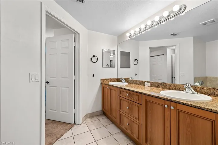 Bathroom featuring double vanity, light tile patterned flooring, and a textured ceiling