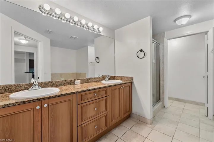 Full bath featuring light tile patterned floors, a stall shower, double vanity, and a textured ceiling