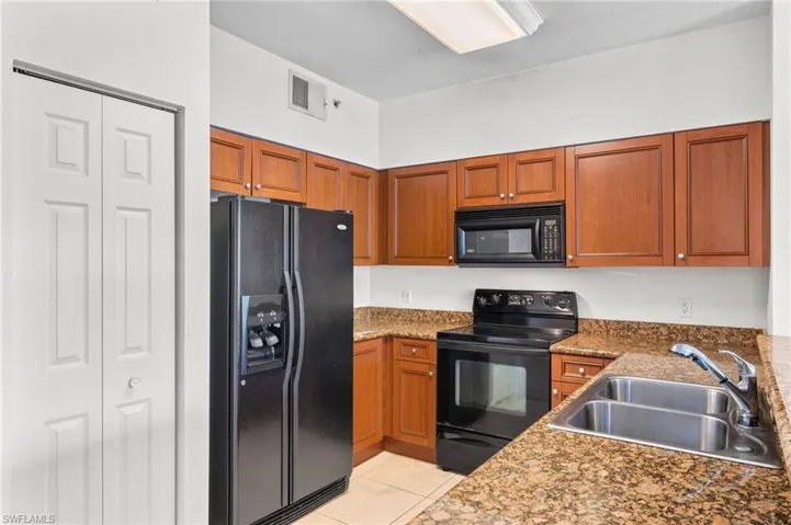 Kitchen with black appliances, brown cabinetry, light tile patterned flooring, and dark stone countertops