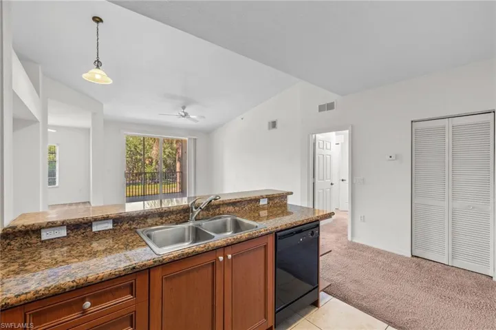 Kitchen with vaulted ceiling, brown cabinets, light carpet, pendant lighting, and black dishwasher