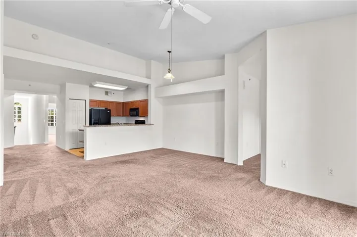 Unfurnished living room featuring light carpet, lofted ceiling, and a ceiling fan
