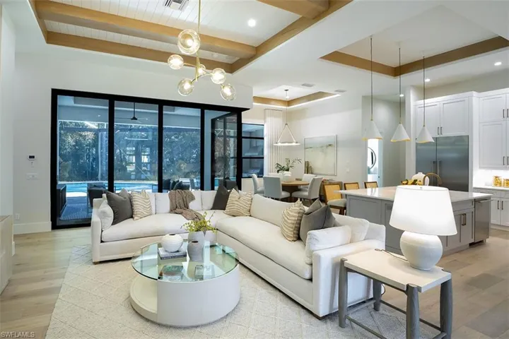 Living area with light wood-style flooring, a raised ceiling, a chandelier, beamed ceiling, and recessed lighting
