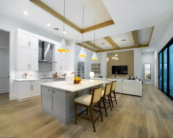 Kitchen with white cabinets, decorative light fixtures, gray cabinets, a kitchen bar, and an island with sink