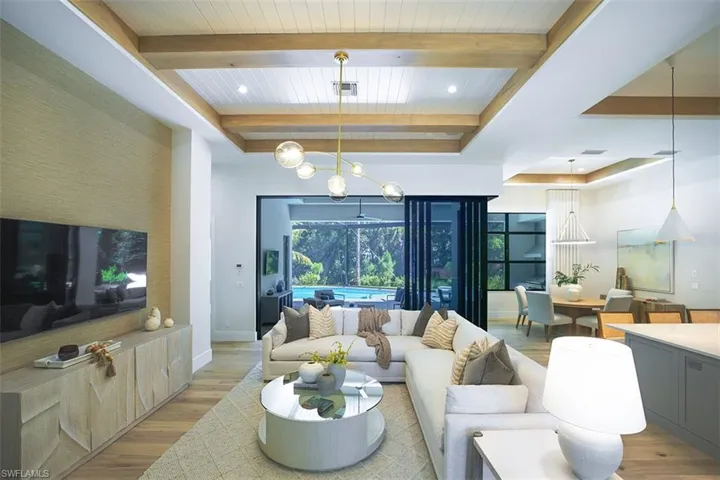 Living room with wood finished floors, a chandelier, a raised ceiling, recessed lighting, and beamed ceiling