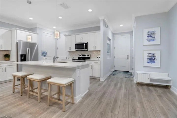 Kitchen with hanging light fixtures, stainless steel appliances, white cabinetry, a kitchen breakfast bar, and a kitchen island with sink