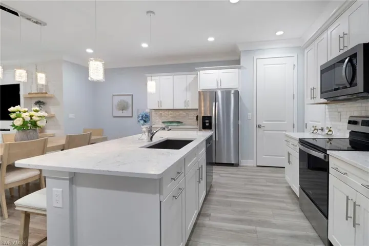Kitchen featuring stainless steel appliances, an island with sink, white cabinets, light stone countertops, and hanging light fixtures