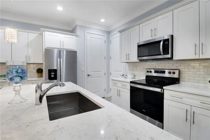 Kitchen with tasteful backsplash, appliances with stainless steel finishes, ornamental molding, pendant lighting, and white cabinetry