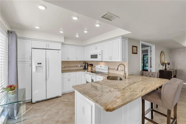 Kitchen featuring kitchen peninsula, white appliances, light stone countertops, and white cabinets