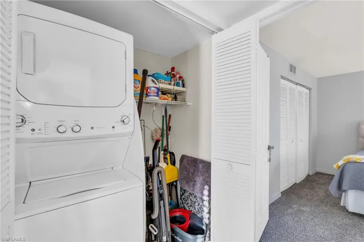 Clothes washing area featuring stacked washer and clothes dryer and carpet