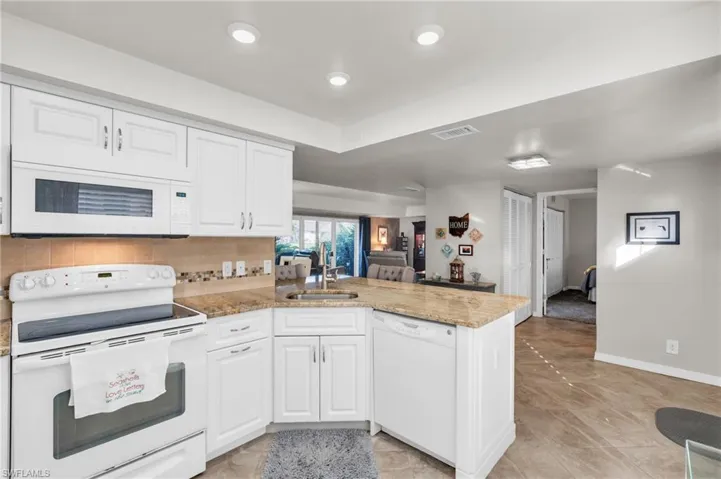 Kitchen featuring white cabinetry, kitchen peninsula, light stone countertops, backsplash, and white appliances