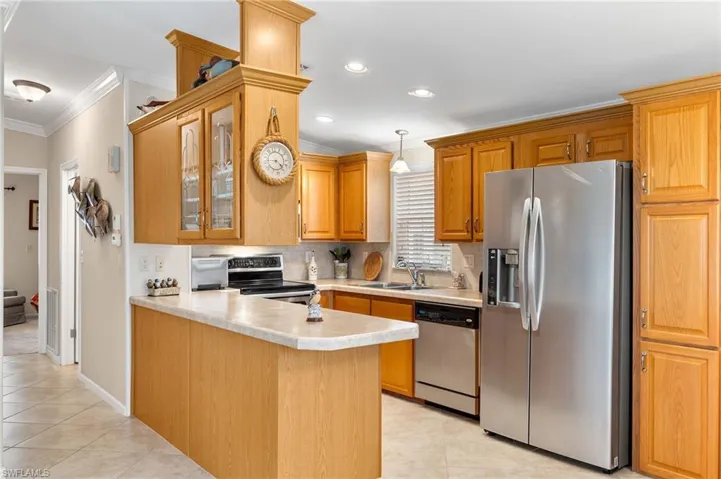 Kitchen with light tile patterned flooring, sink, kitchen peninsula, stainless steel appliances, and crown molding